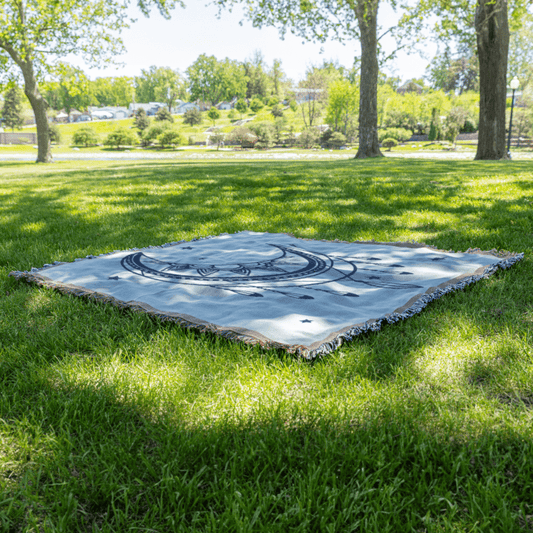 Mystical Moon Woven Blanket laid on grass outdoors, crescent moon and star pattern ideal for stargazing or meditation rituals.