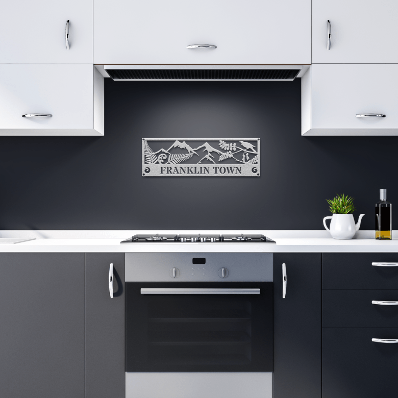 Silver wall art with symbolic Māori fern and manu, displayed in a modern dark kitchen for a serene cultural touch