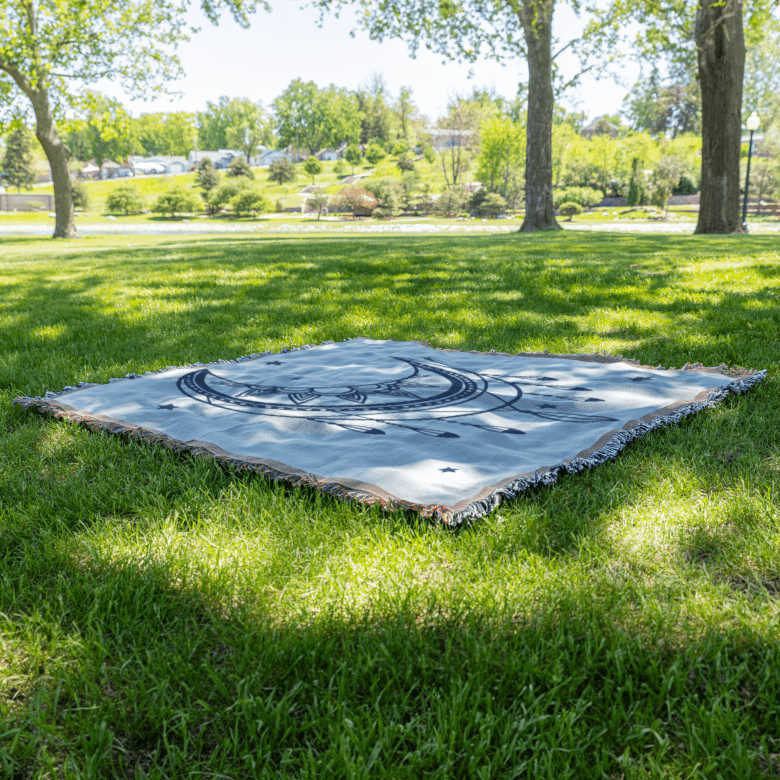 Mystical Moon Woven Blanket laid on grass outdoors, crescent moon and star pattern ideal for stargazing or meditation rituals.